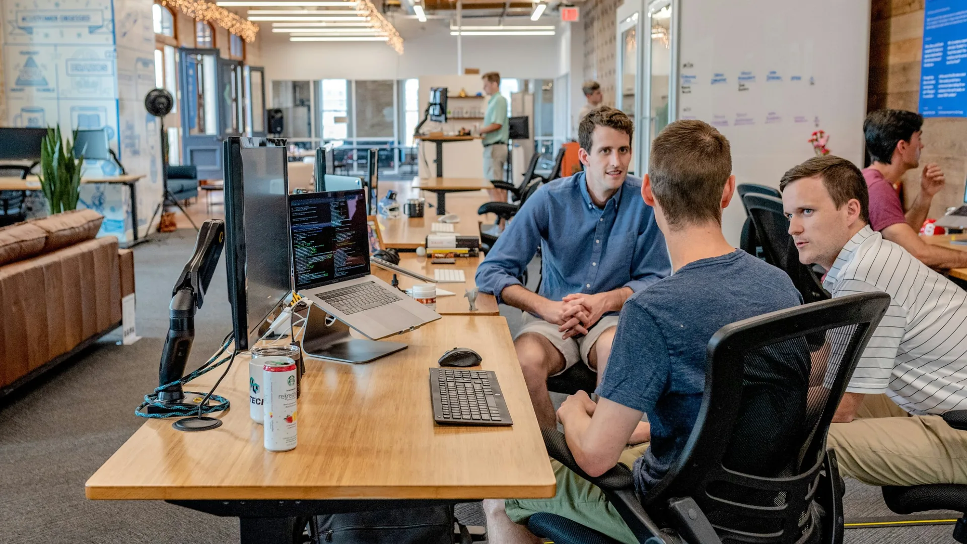 Three coworkers having a conversation around a desk in an open office